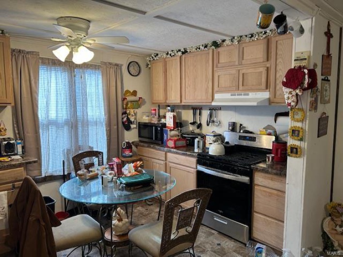 Kitchen featuring dark countertops, light brown cabinetry, ventilation hood, and gas stove