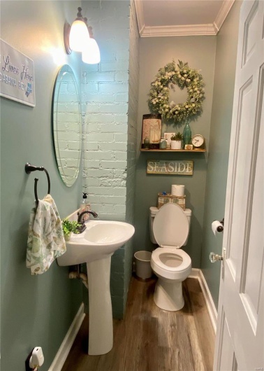 Half bathroom with toilet, brick wall, wood finished floors, baseboards, and crown molding