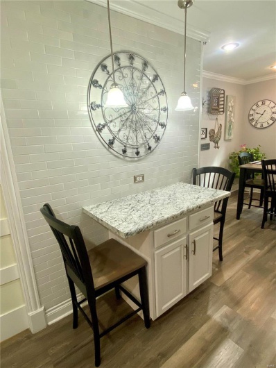 Kitchen featuring light stone counters, dark wood finished floors, hanging light fixtures, ornamental molding, and white cabinetry