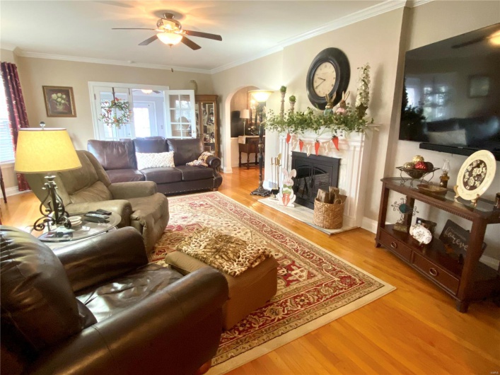 Living room with ornamental molding, arched walkways, a fireplace, and wood floors