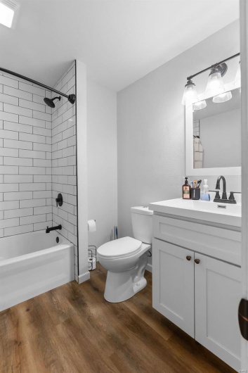 Full bathroom with tiled shower / bath, vanity, hardwood / wood-style floors, and toilet