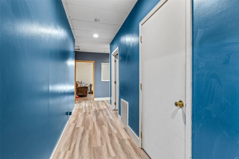 Hallway featuring light wood-type flooring, visible vents, baseboards, and a drop ceiling