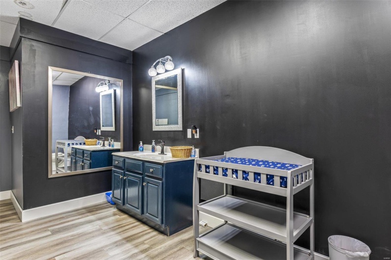 Bathroom featuring a paneled ceiling, wood finished floors, two vanities, a sink, and baseboards