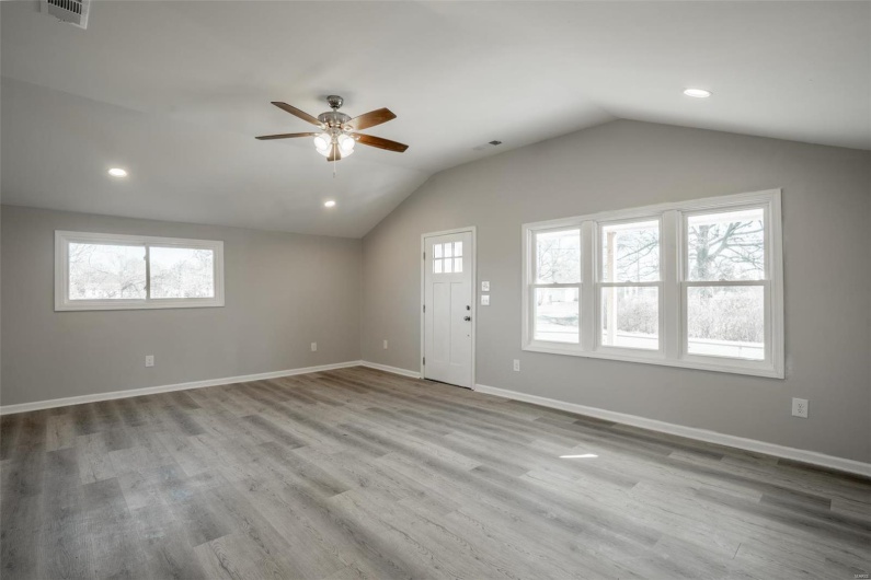 Spare room featuring vaulted ceiling, plenty of natural light, wood finished floors, and visible vents
