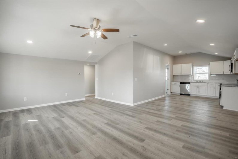 Unfurnished living room featuring vaulted ceiling, light wood-type flooring, visible vents, and baseboards