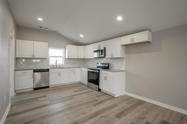 Kitchen with visible vents, lofted ceiling, stainless steel appliances, light wood-style floors, and a sink