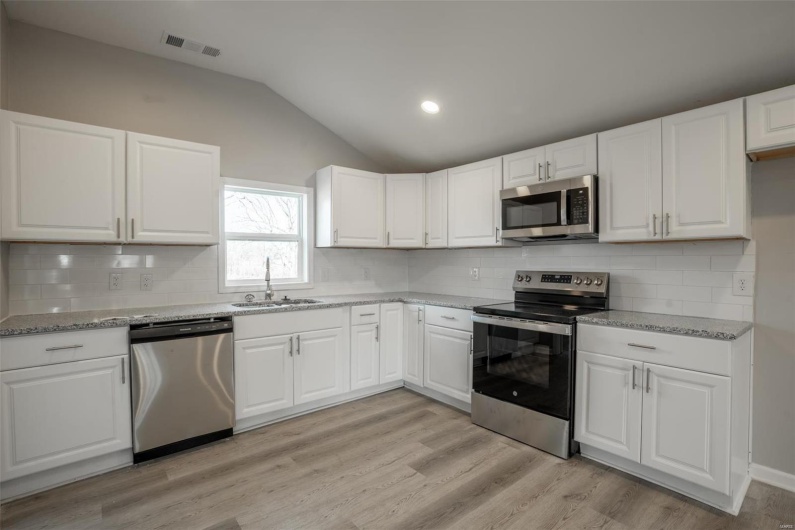 Kitchen featuring stainless steel appliances, lofted ceiling, visible vents, light wood-style flooring, and a sink