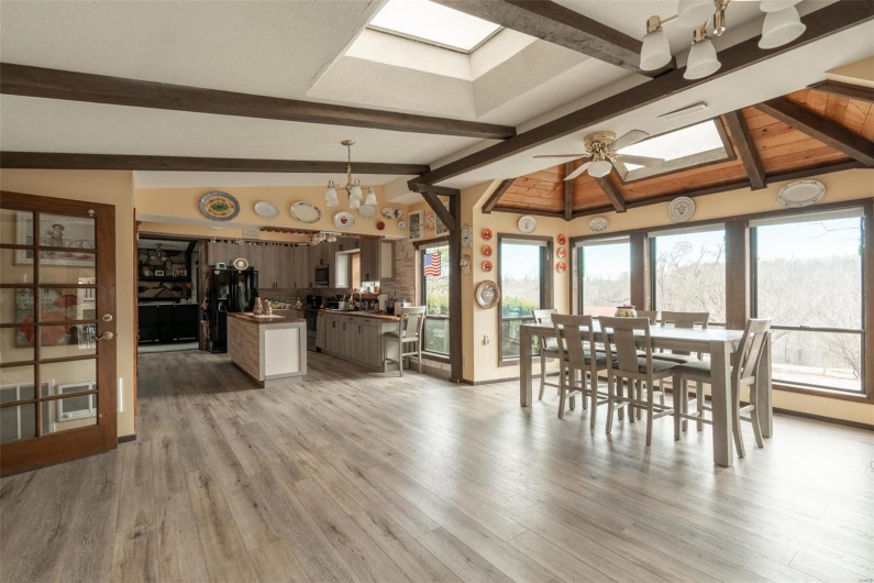 Dining space with lofted ceiling with skylight, visible vents, light wood-style flooring, and ceiling fan with notable chandelier