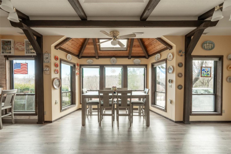 Unfurnished dining area featuring baseboards, a healthy amount of sunlight, wood finished floors, and vaulted ceiling with beams