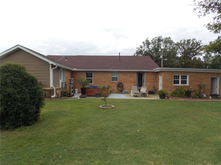 Rear view of property with a patio area, a lawn, a hot tub, and brick siding