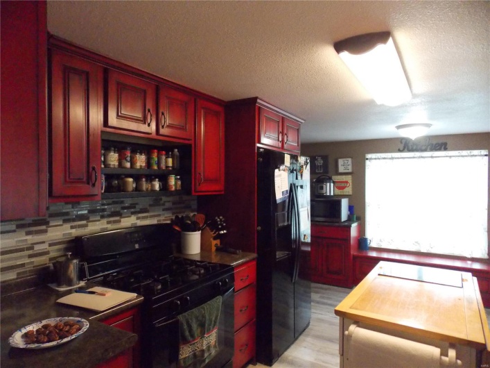 Kitchen featuring black appliances, tasteful backsplash, a textured ceiling, reddish brown cabinets, and light wood-style floors