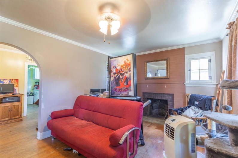 Living area with arched walkways, a brick fireplace, light wood-type flooring, and ornamental molding