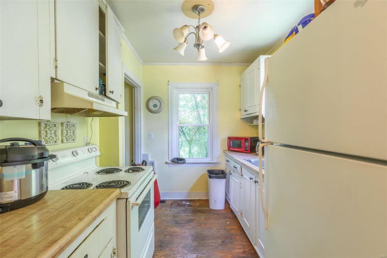 Kitchen with white appliances, white cabinets, crown molding, and under cabinet range hood