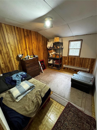 Bedroom with a baseboard heating unit, wooden walls, and a wainscoted wall