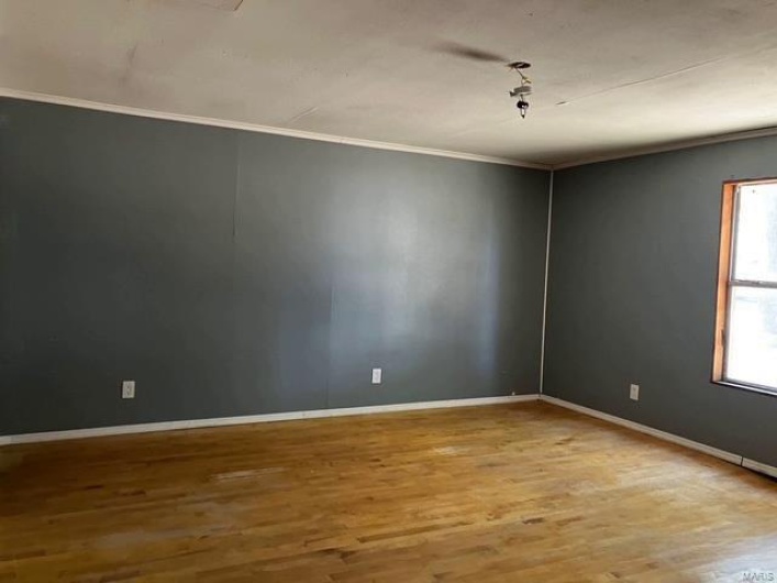 Empty room with wood finished floors, baseboards, and ornamental molding