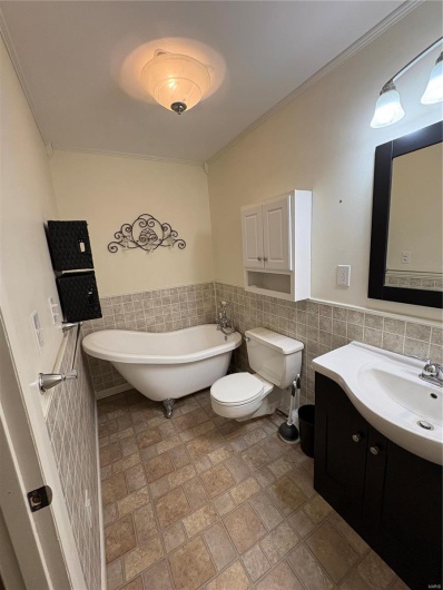 Bathroom featuring toilet, tile walls, ornamental molding, a bath, and vanity