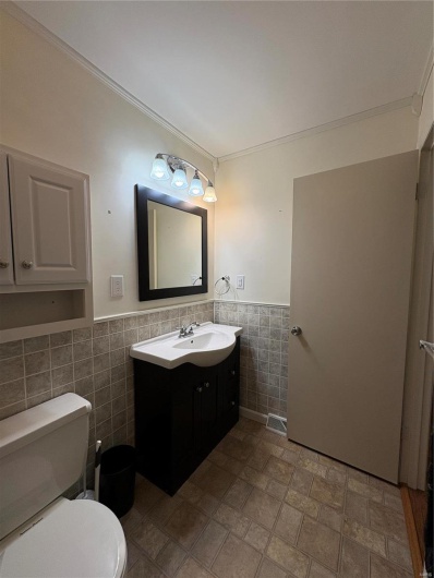 Bathroom with tile walls, toilet, vanity, and crown molding