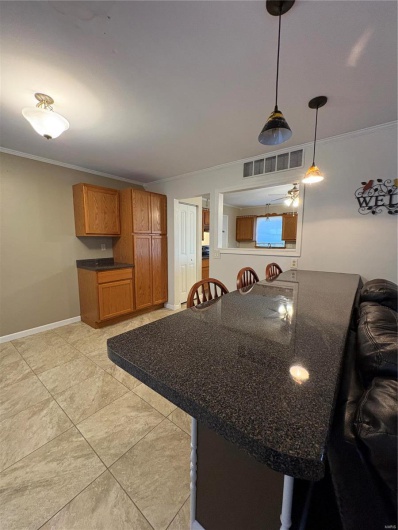 Kitchen with kitchen peninsula, a kitchen breakfast bar, hanging light fixtures, light tile patterned floors, and ornamental molding