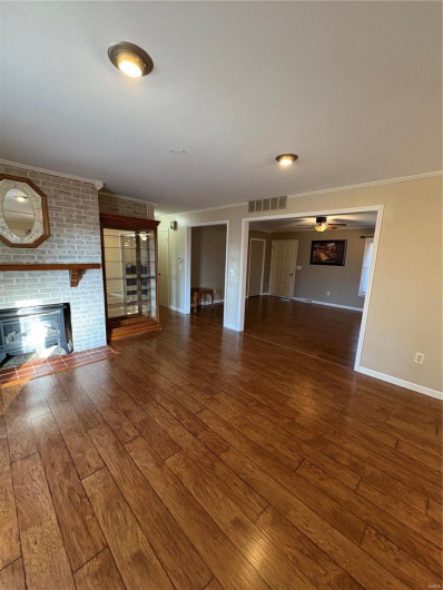 Unfurnished living room featuring ceiling fan, a brick fireplace, and dark wood-type flooring