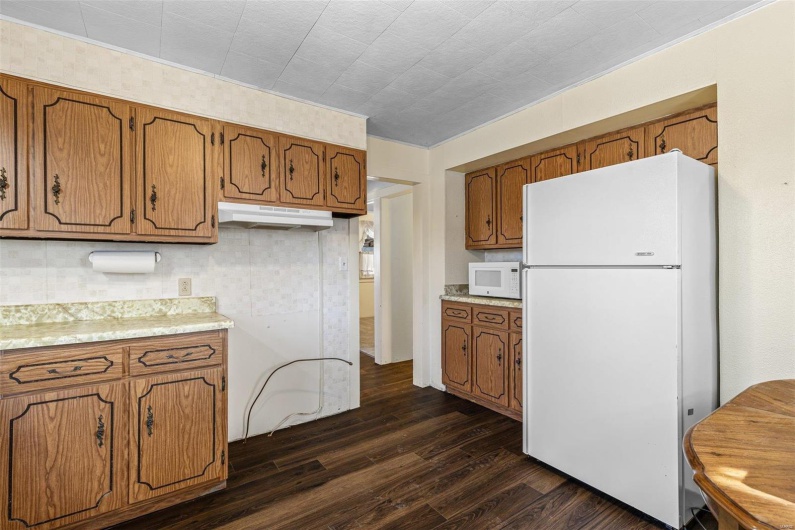 Kitchen featuring under cabinet range hood, white appliances, dark wood-type flooring, and brown cabinetry