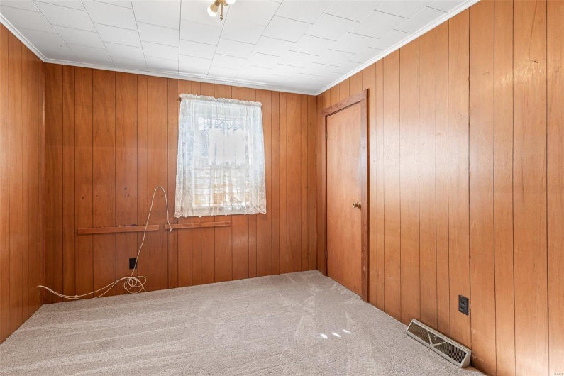 Unfurnished room featuring visible vents, wood walls, and carpet