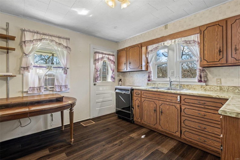 Kitchen featuring brown cabinets, a sink, plenty of natural light, light countertops, and dark wood-style flooring