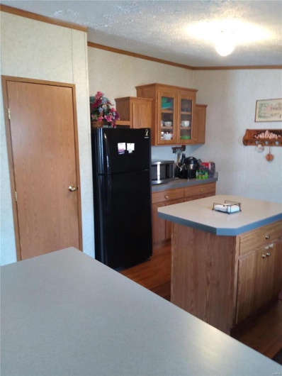 Kitchen featuring brown cabinets, stainless steel microwave, freestanding refrigerator, crown molding, and glass insert cabinets