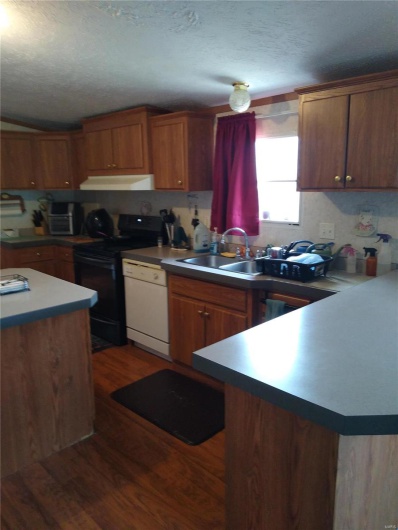 Kitchen featuring electric range, under cabinet range hood, a textured ceiling, dark wood-style floors, and dishwasher