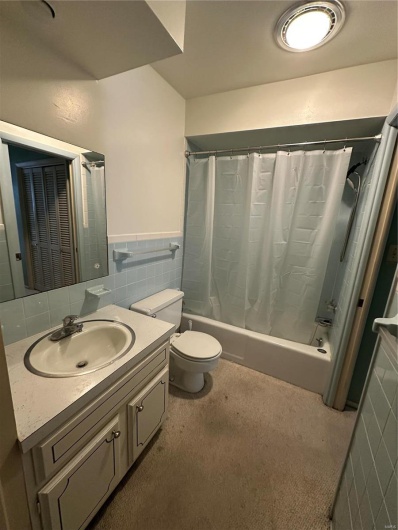 Full bathroom featuring vanity, shower / bath combo with shower curtain, wainscoting, tile walls, and toilet