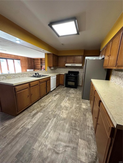 Kitchen with stove, light wood-style floors, dishwasher, fridge, and tasteful backsplash