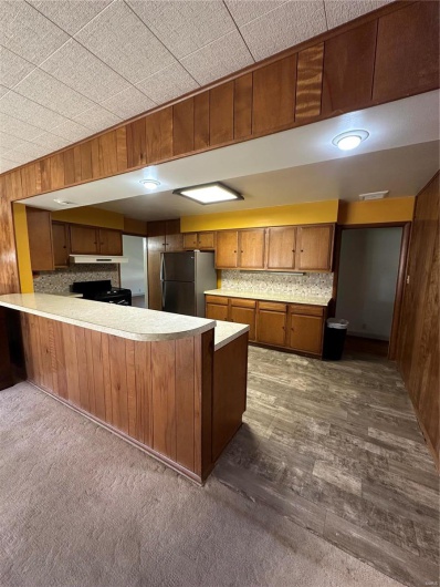 Kitchen featuring wood walls, decorative backsplash, a peninsula, brown cabinetry, and fridge