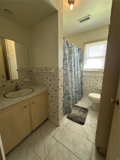 Bathroom with visible vents, tile walls, toilet, marble finish floor, and vanity