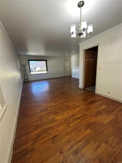 Empty room featuring a notable chandelier, ornamental molding, and dark wood-style flooring