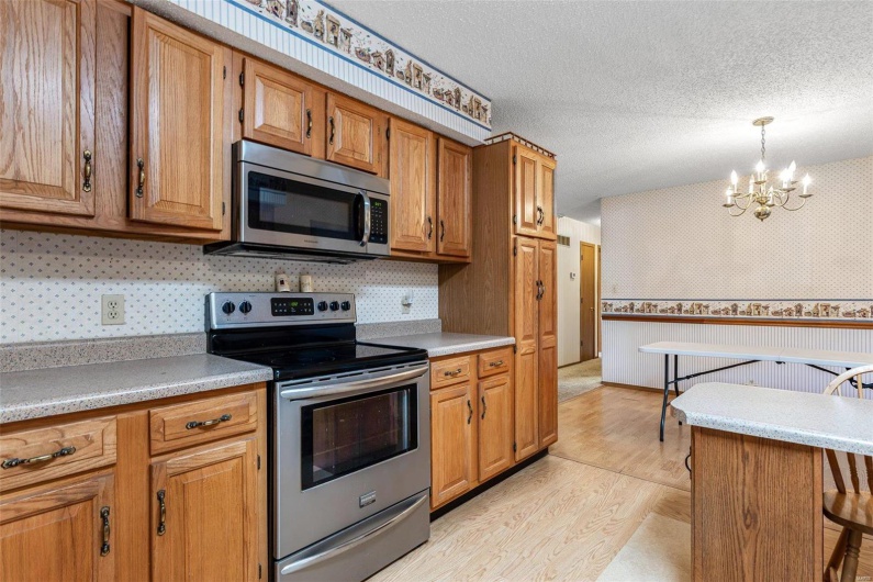 Kitchen with light wood finished floors, stainless steel appliances, a textured ceiling, brown cabinets, and a chandelier