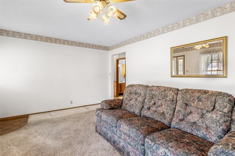 Carpeted living room featuring a textured ceiling, baseboards, and ceiling fan
