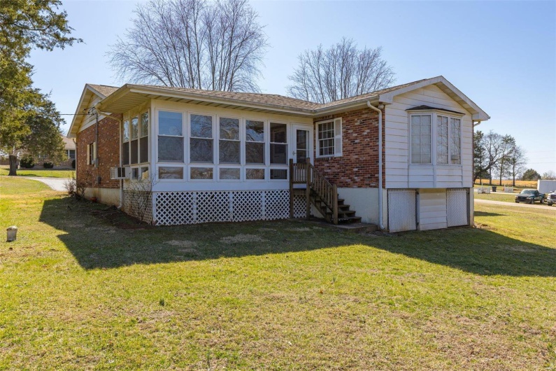 Back of property featuring brick siding, a lawn, cooling unit, and a sunroom