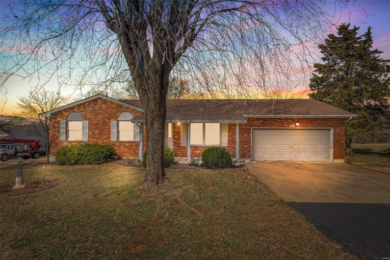 Single story home featuring brick siding, an attached garage, a front lawn, roof with shingles, and driveway