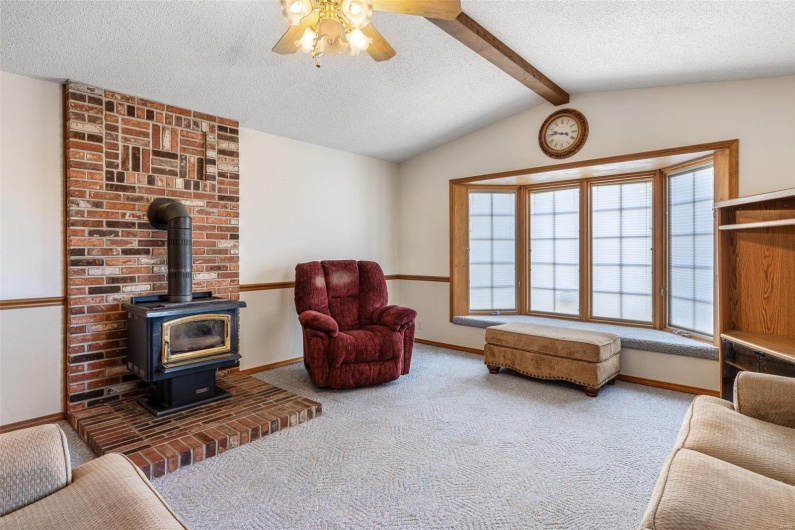 Carpeted living area with baseboards, lofted ceiling with beams, a wood stove, ceiling fan, and a textured ceiling