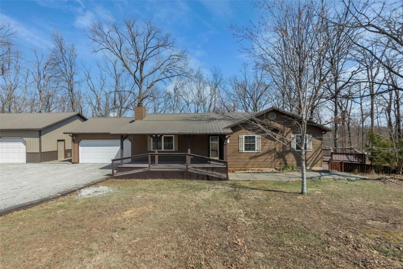 Single story home featuring covered porch, a chimney, metal roof, a garage, and driveway