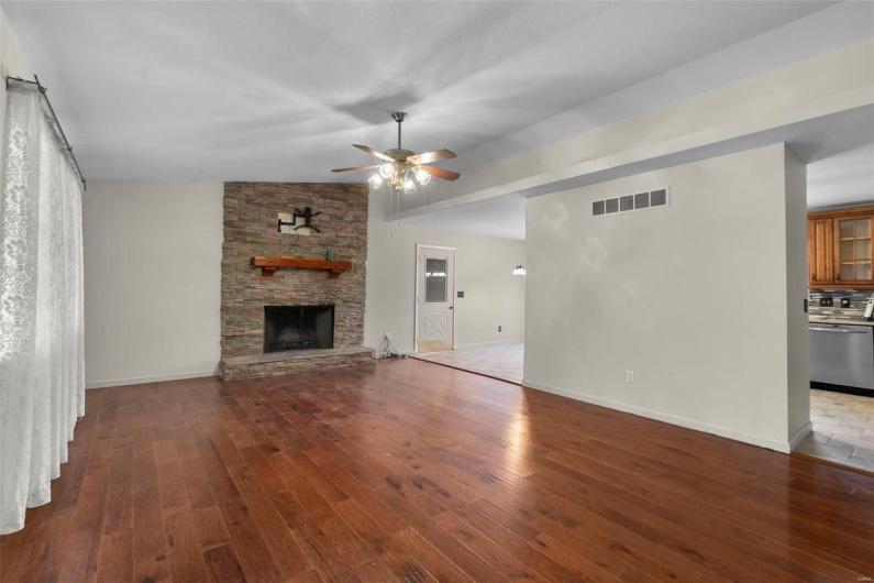 Unfurnished living room with visible vents, baseboards, ceiling fan, hardwood / wood-style floors, and a stone fireplace