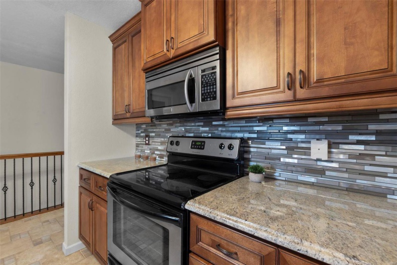 Kitchen featuring backsplash, light stone countertops, brown cabinets, stone finish floor, and stainless steel appliances