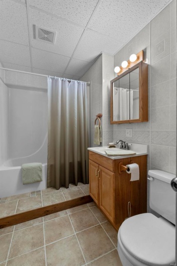 Bathroom featuring vanity, visible vents, a drop ceiling, tile walls, and toilet