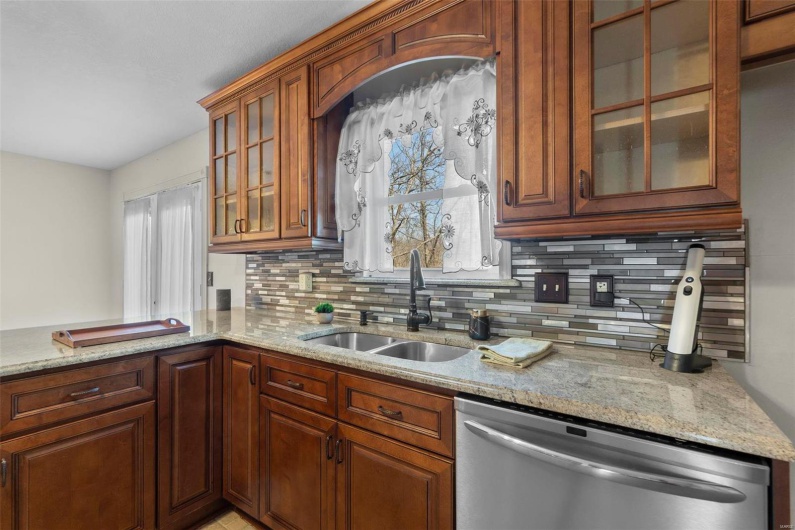 Kitchen with light stone counters, a sink, decorative backsplash, glass insert cabinets, and stainless steel dishwasher
