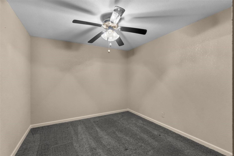 Spare room featuring dark carpet, baseboards, and a ceiling fan