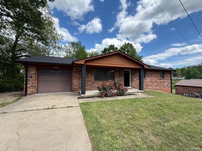 Ranch-style home featuring covered porch, an attached garage, concrete driveway, a front lawn, and brick siding
