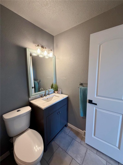 Bathroom featuring toilet, vanity, a textured ceiling, tile patterned floors, and a textured wall