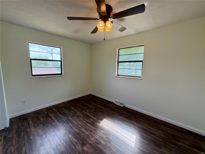 Empty room featuring dark wood finished floors, a wealth of natural light, visible vents, and baseboards
