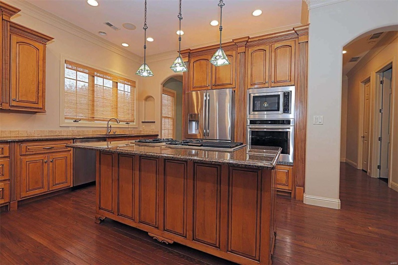 Kitchen with ornamental molding, dark wood-type flooring, a center island, and stainless steel appliances