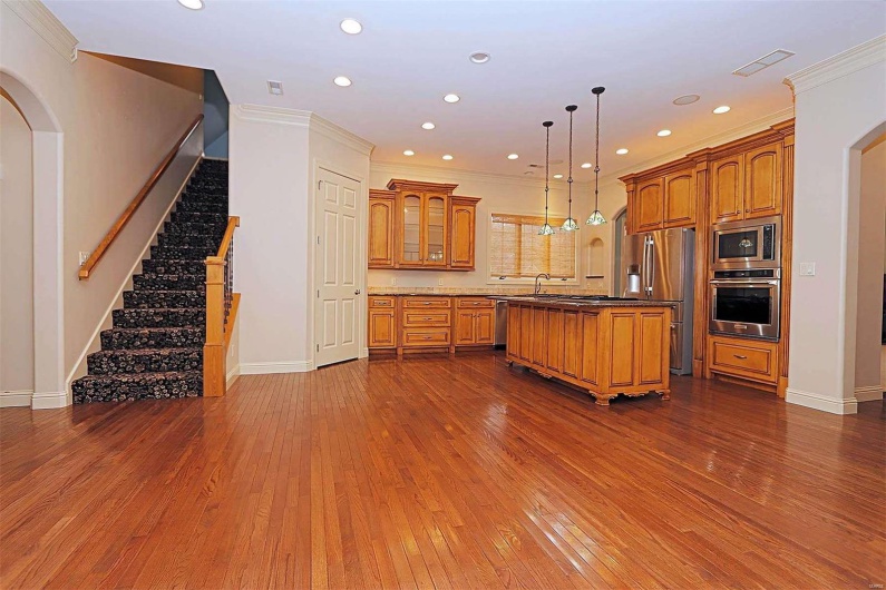 Kitchen with hanging light fixtures, a kitchen island, appliances with stainless steel finishes, dark hardwood / wood-style floors, and crown molding