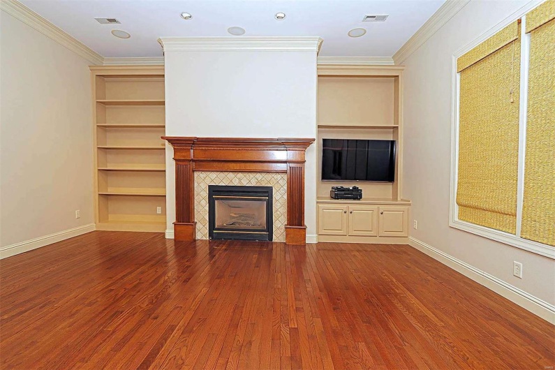 Unfurnished living room featuring a tiled fireplace, built in features, ornamental molding, and hardwood / wood-style floors